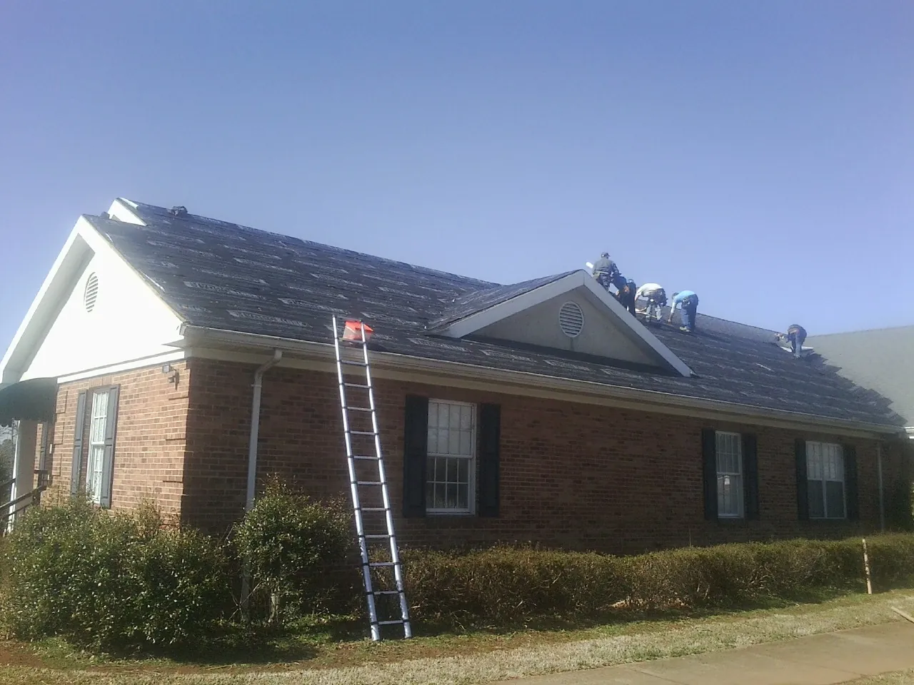 Crew tearing shingles off a brick ranch roof with a ladder set — Metal Roof Repair work by our crew in Mount Vernon